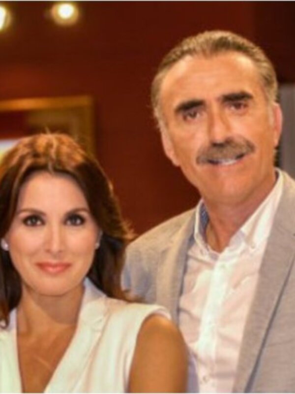 Dos personas posan en un entorno profesional, probablemente en un estudio de televisión o producción. La imagen muestra a una mujer con cabello largo y una persona masculina con barba, ambos sonrientes. La escena sugiere un momento de camaradería o presentación en un programa televisivo.