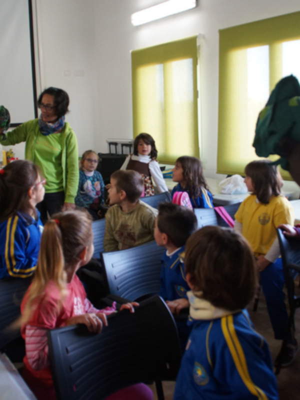 Niños escuchando a una persona adulta en una sala de conferencias, con una pantalla proyector en el fondo.