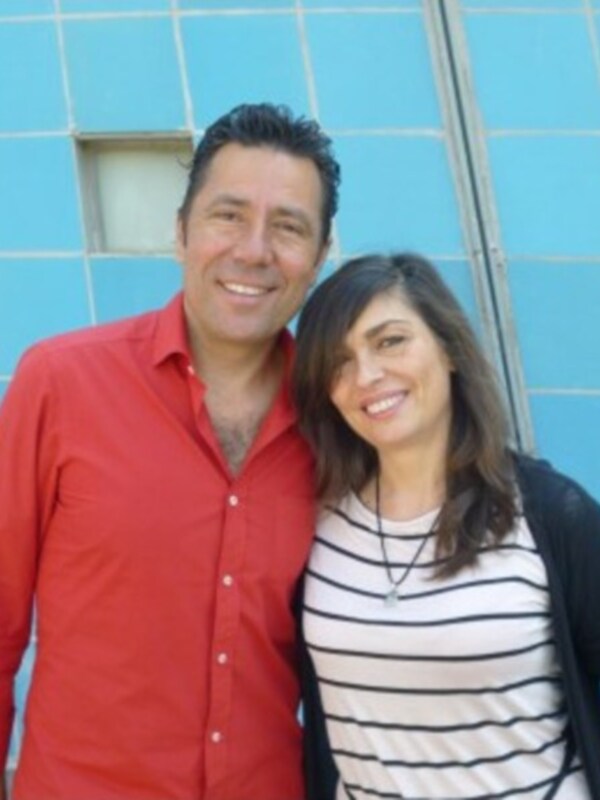 Un hombre y una mujer sonrientes en frente de un edificio azul con ventanas.