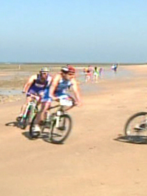 Competencia de bicicleta en la playa, con ciclistas en acción y público observando.