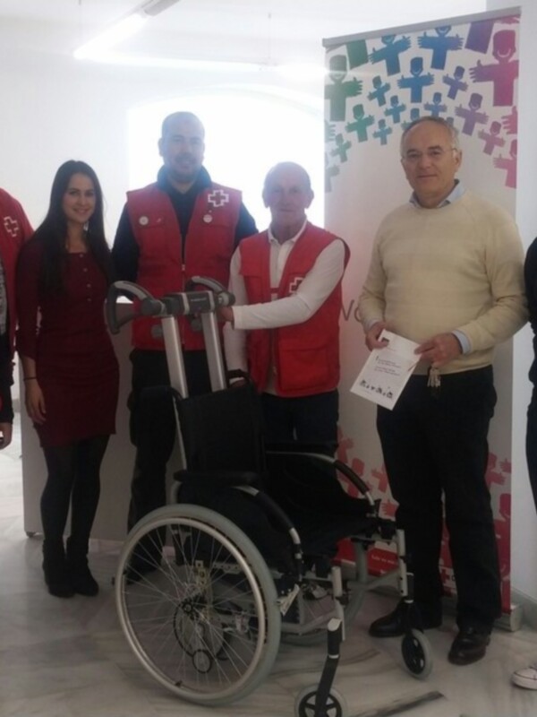 Equipo de voluntarios en un evento benéfico, con una silla de ruedas y un cartel informativo.