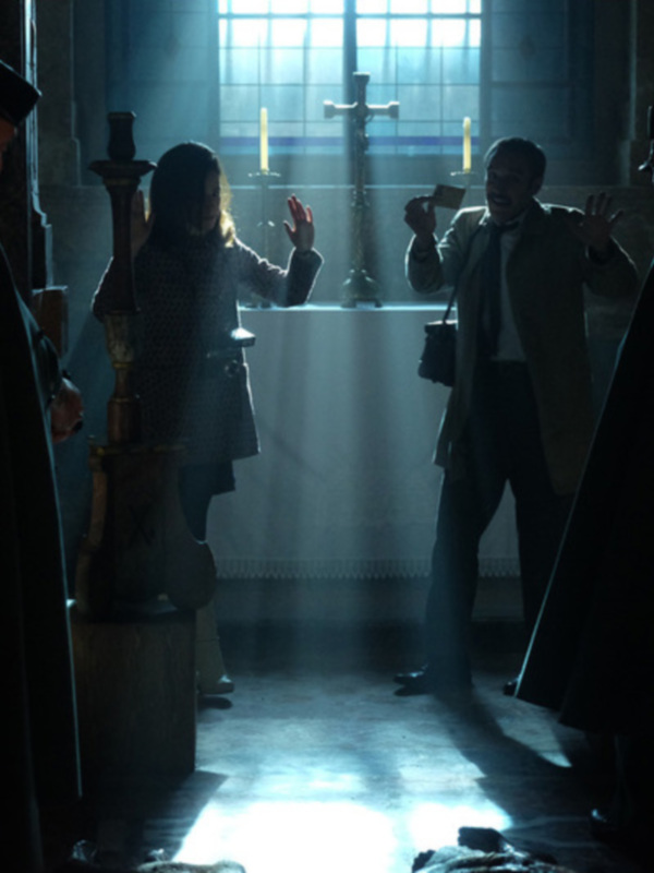 Una escena oscura y misteriosa en un interior oscuro, con una figura femenina y tres hombres vestidos de manera formal. La luz se filtra a través de una ventana, iluminando el lugar y creando sombras. La atmósfera sugiere un ambiente de intriga o suspense.