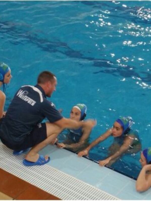 Entrenamiento de waterpolo infantil en una piscina. Los niños escuchan atentamente a su entrenador.
