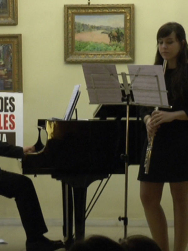 Un pianista y una flautista interpretan en un recital de música clásica, con obras de Debussy en el escenario.