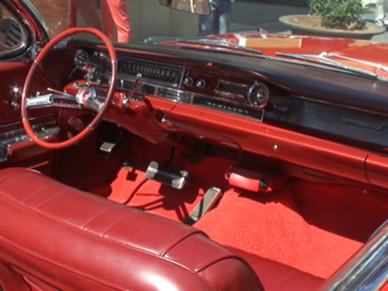 Interior de un clásico automóvil rojo con detalles en cuero y acabados metálicos.