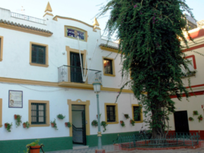 Fachada de un edificio colonial con ventanas decoradas, una escalera y una gran planta trepadora en el balcón.