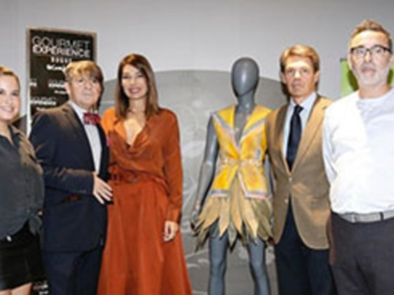 Una imagen de una presentación en un evento gastronómico, con personas posando frente a un cartel que dice 'Gourmet Experience'.