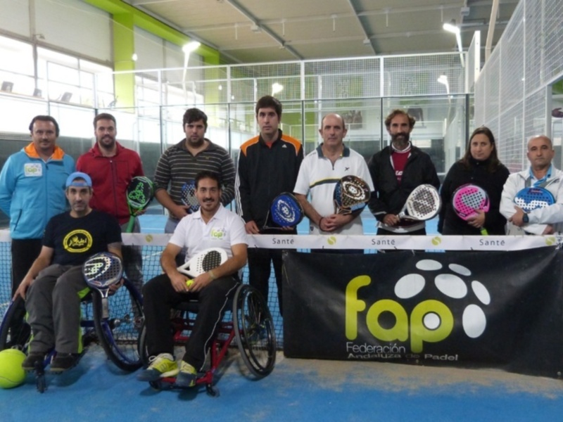 Gente en sillas de ruedas posando con raquetas de padel y una bandera FAP en un entorno deportivo.