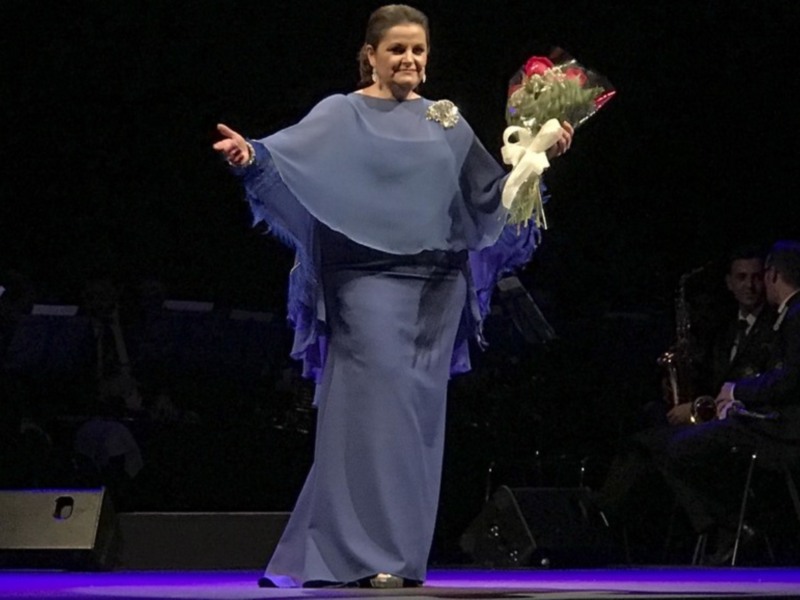 Una mujer en un vestido azul con flores en la mano, posando en un escenario.