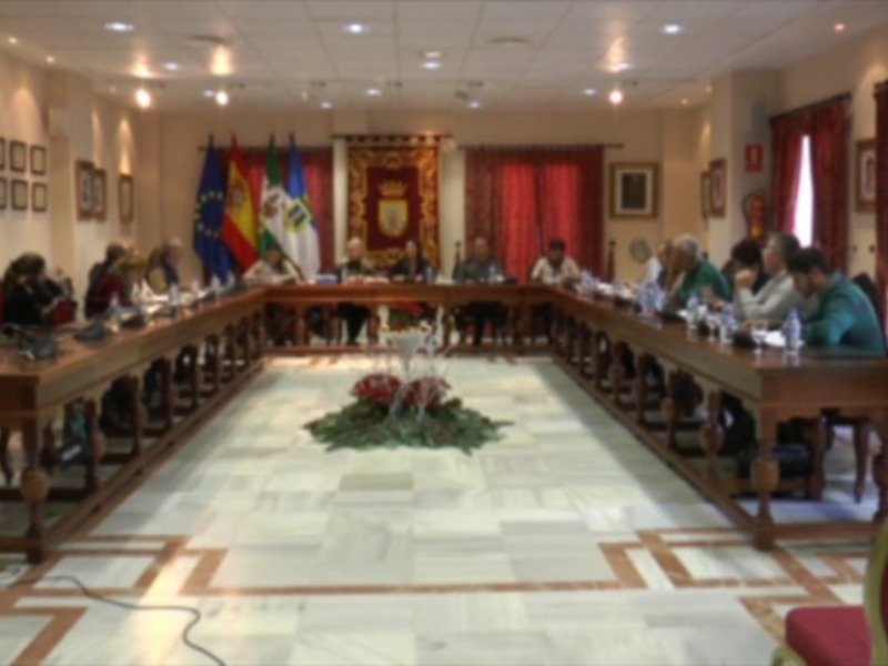Sala de reuniones con una mesa redonda, personas sentadas y banderas en el fondo.