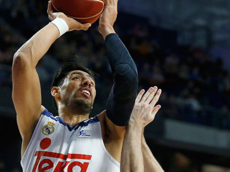 Un jugador de baloncesto en acción, con el balón en la mano, durante un partido en un estadio lleno de espectadores.