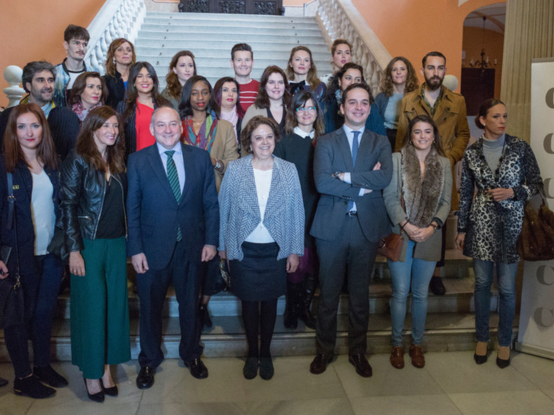 Una foto de grupo de personas en un salón elegante, con una señora en el centro y una pancarta con el texto 'CODE41' en el fondo.