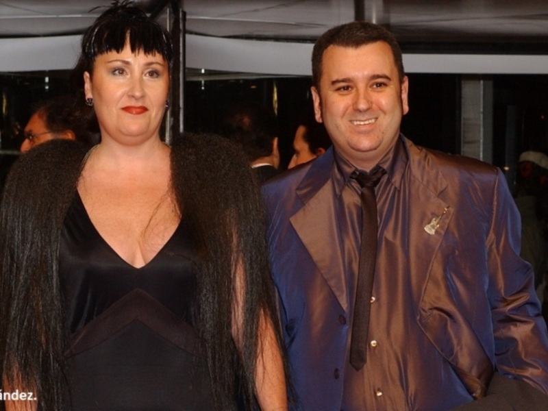 Una pareja en una fiesta formal, el hombre está sonriendo mientras la mujer mira hacia otro lado.