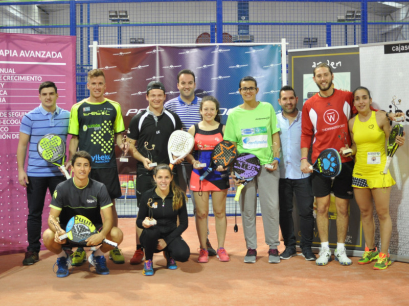 Equipo de padel posando en una cancha con raquetas y uniformes coloridos.