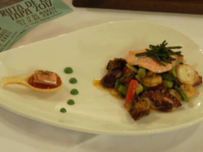 Una ensalada de pescado y verduras en un plato blanco, acompañada por una hoja de papel verde con texto.