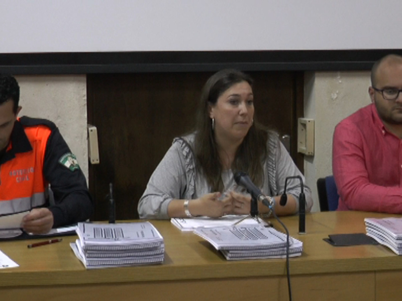 Tres personas sentadas en una mesa con papeles y un micrófono, posiblemente en una conferencia o reunión formal.