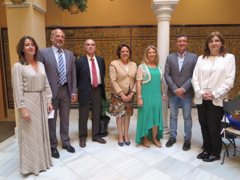 Grupo de personas posando para una foto en un entorno formal con azulejos y una planta colgante en el fondo.