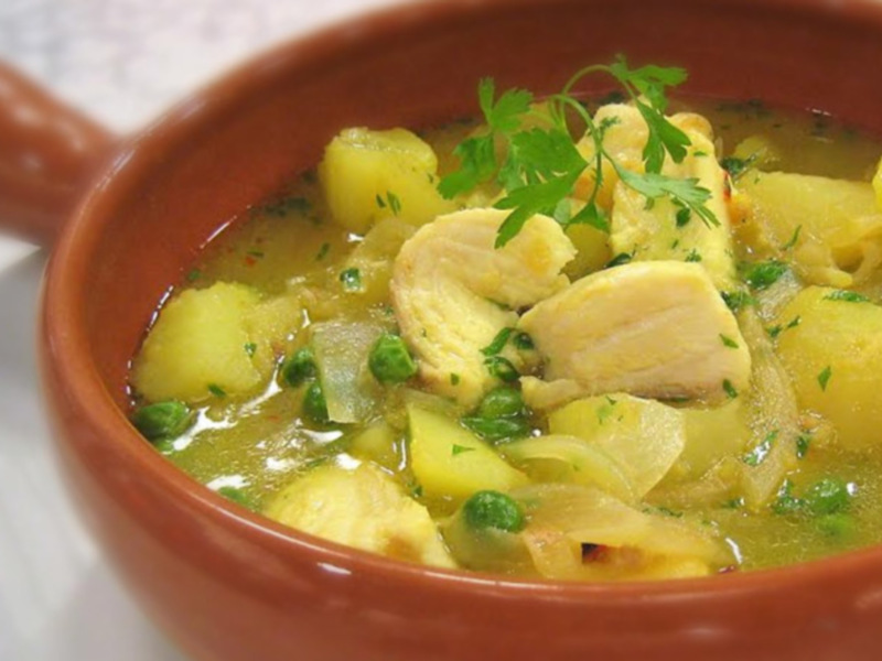 Un delicioso guiso de pollo y patatas, acompañado de guisantes verdes, en un tazón de barro rojo, listo para ser disfrutado.