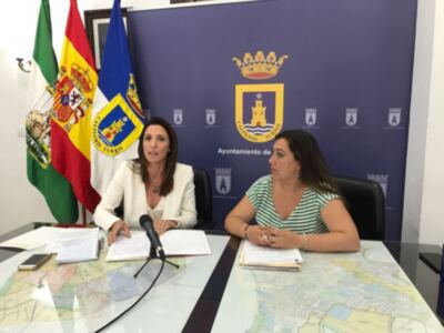 Dos mujeres sentadas en una mesa con documentos y un mapa, junto a banderas de España y la provincia de Cádiz.