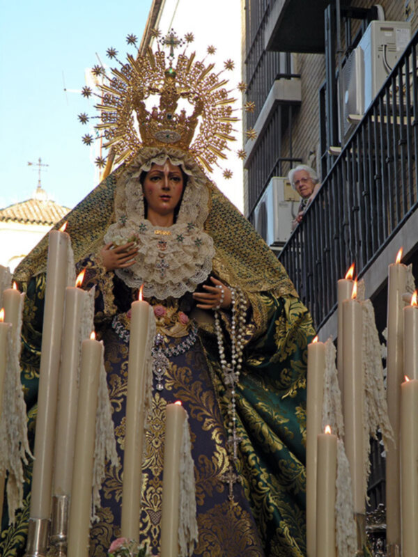 Procesión religiosa con imagen de la Virgen María rodeada de velas en una calle urbana.