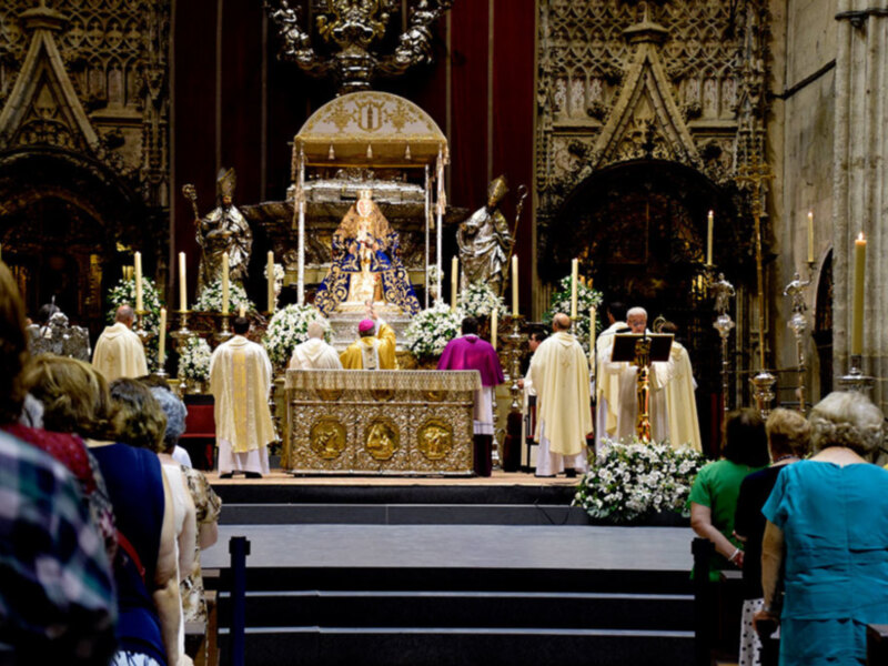 Una ceremonia religiosa en una iglesia con una imagen central dorada, velas y un coro de personas vestidas con vestidos largos. La atmósfera es reverente y solemn.