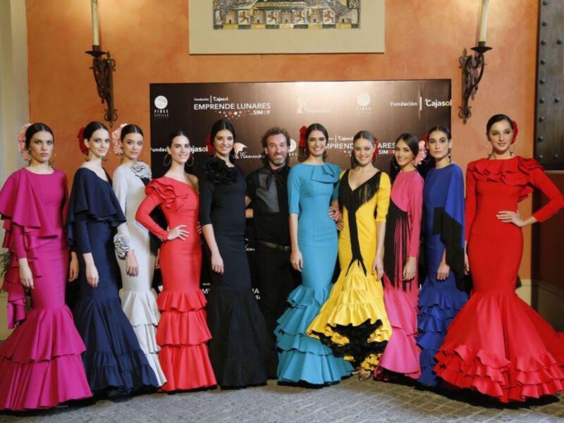 Modelos posan con vestidos de flamenca de diferentes colores y estilos en una presentación de moda.