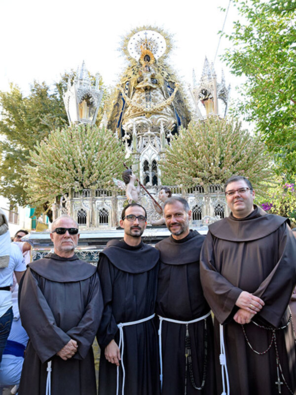 Monjes en una procesión religiosa con una imagen de la Virgen en el fondo.