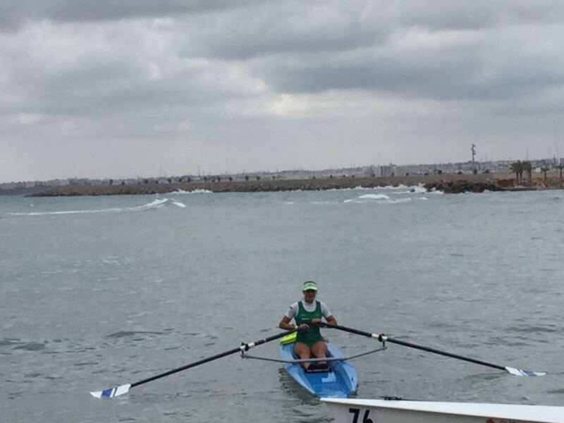 Una persona remando en una canoa en el mar, con el horizonte y la costa en el fondo.
