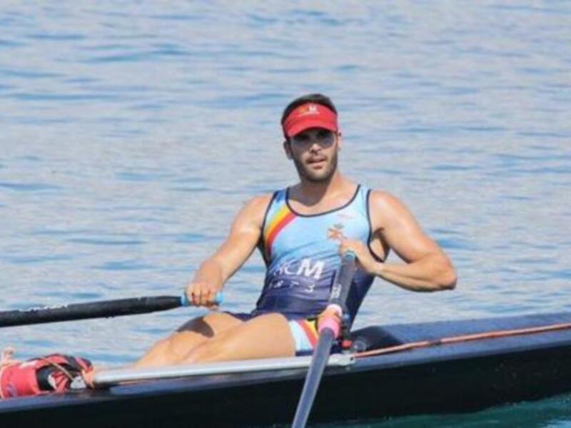 Atleta practicando remo en un lago tranquilo, con un chaleco de competición y remo en mano.