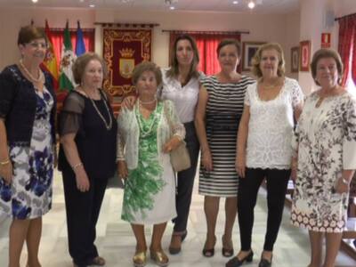 Señoras de diferentes edades y estilos vestidos, posando juntas en un ambiente decorado con banderas y una gran bandera.