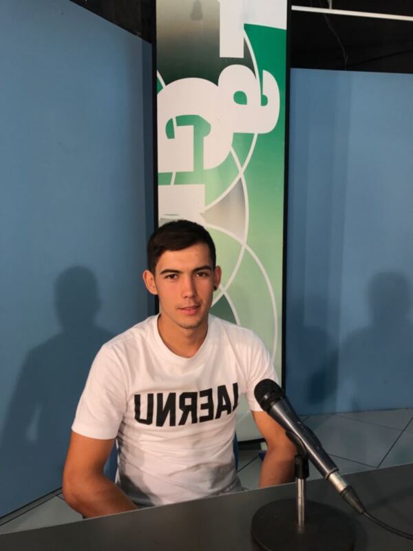Persona joven en estudio de radio con microfono y fondo de diseño gráfico.