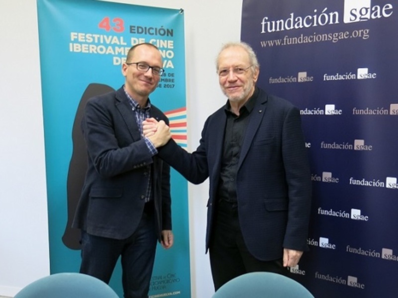 Dos hombres saludándose en un evento de la Fundación SGAE, con banners de la 43 edición del Festival de Cine Iberoamericano en el fondo.