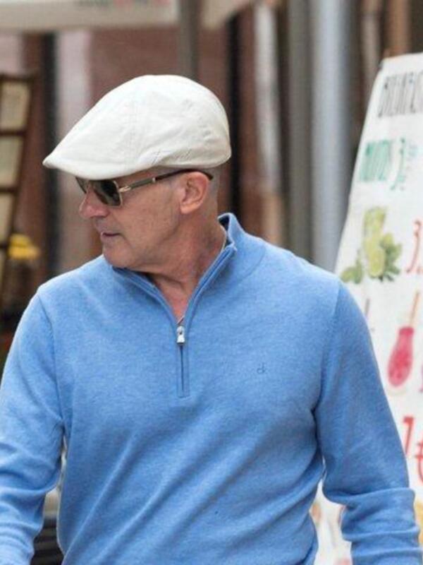 Man wearing a blue sweater and a white cap walking outdoors.