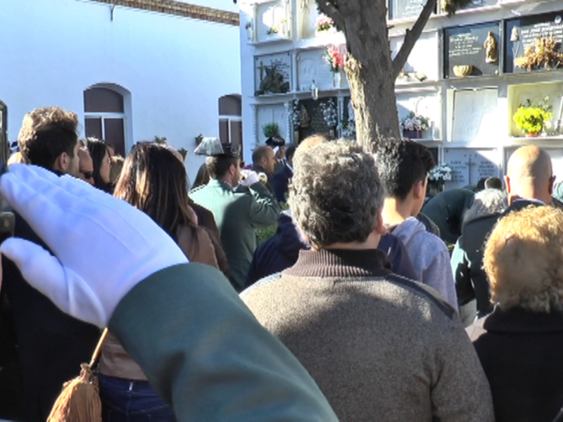 Una multitud de personas en un cementerio, con una mano levantada en un saludo militar, frente a un mausoleo con flores y estatuas.