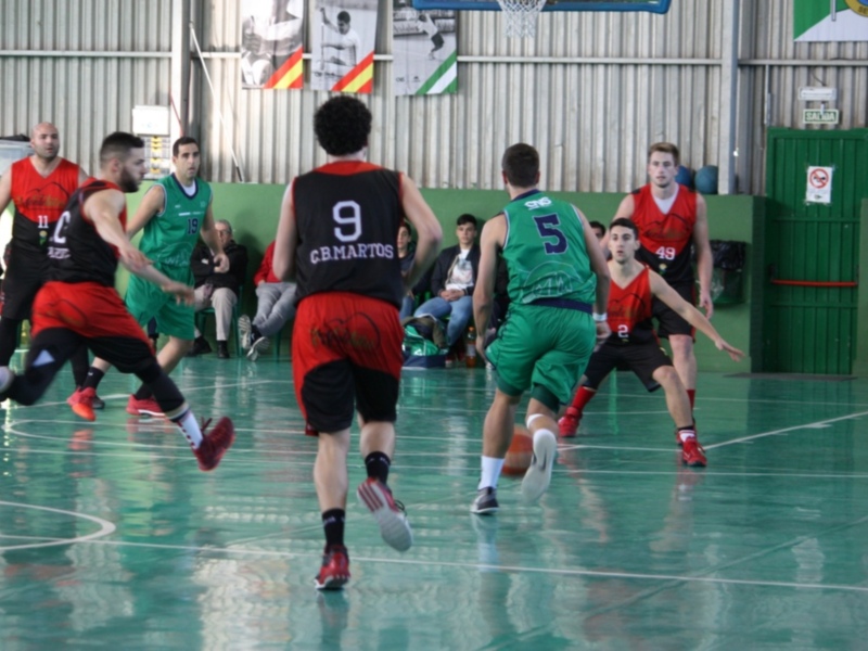 Jugadores de baloncesto en acción durante un partido en un gimnasio con banderas y espectadores observando en el fondo.