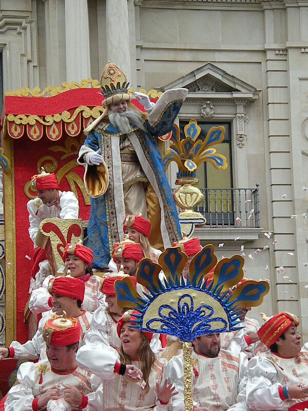 Desfile de carnaval con personajes en trajes tradicionales y disfraces coloridos, frente a un edificio histórico.
