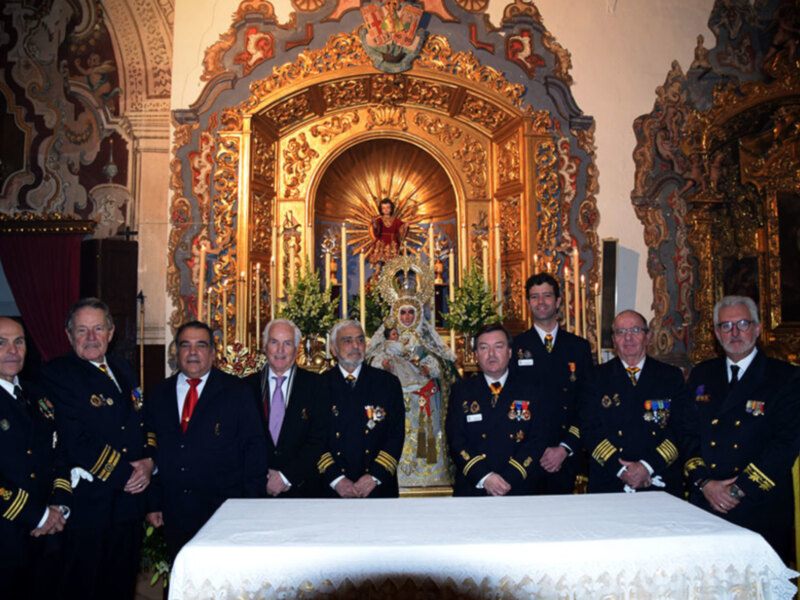 Una imagen de oficiales militares posando frente a un altar decorado con velas y flores, con una figura religiosa en el centro.