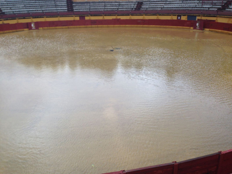 Interior de una plaza de toros vacía con el suelo mojado y las gradas desiertas.