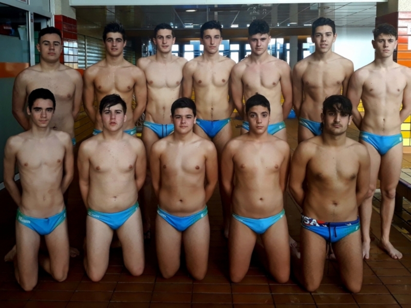 Equipo de natación masculina posando en el gimnasio de natación, todos vestidos con trajes de baño azules.