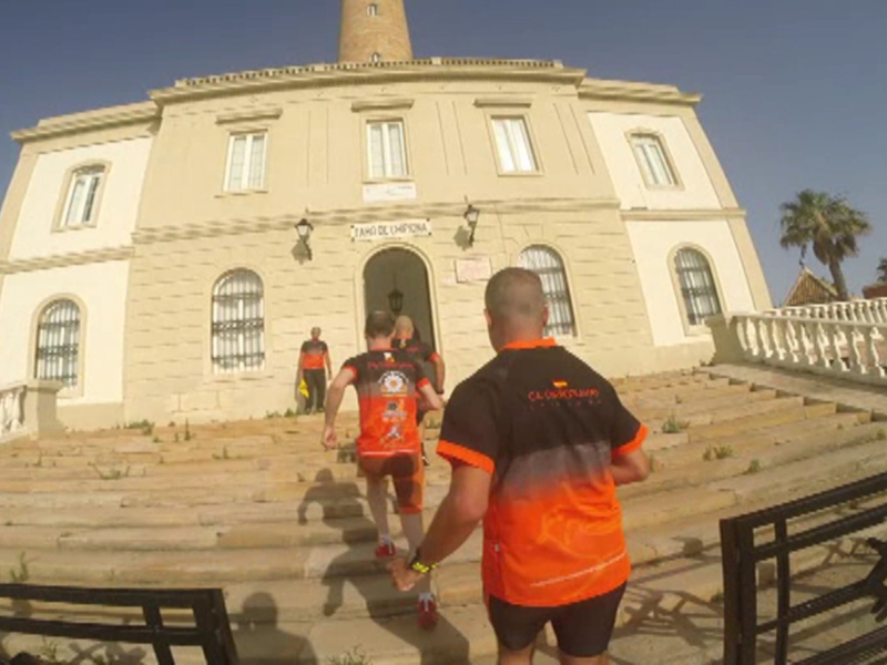 Atletas en camisetas de running subiendo las escaleras del Faro de Chipiona bajo un cielo despejado.