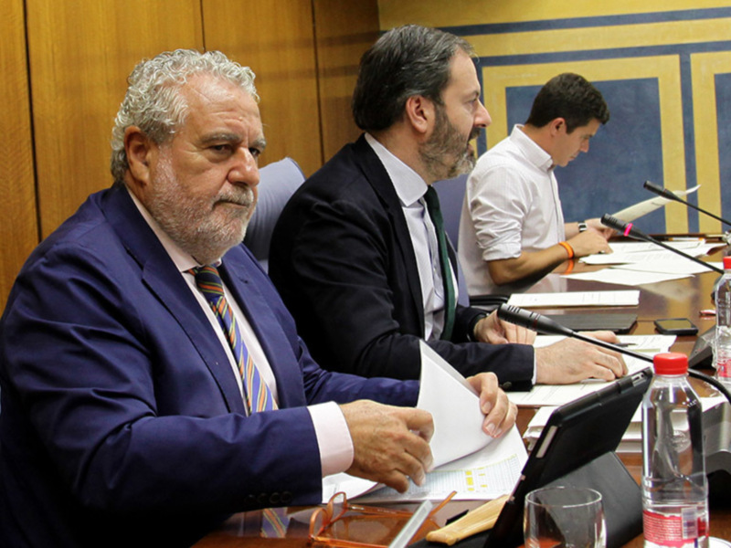 Tres hombres sentados en una sala de conferencias, uno de ellos está sosteniendo un documento mientras los otros dos observan.