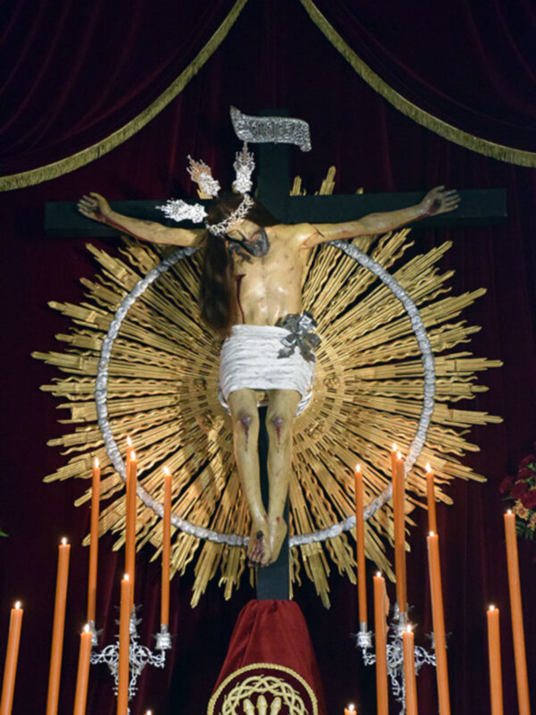 Representación del Cristo crucificado con un halo dorado y velas en primer plano.