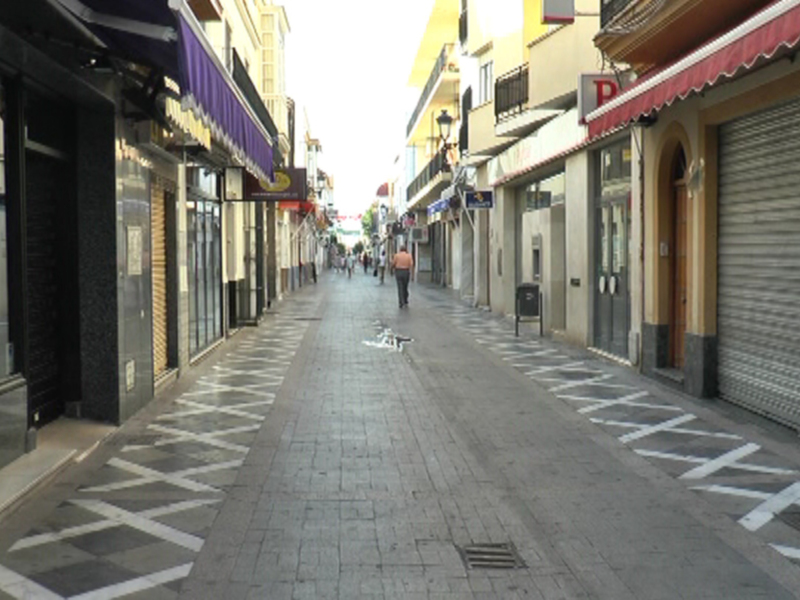 Calle vacía con tiendas cerradas y gente caminando.
