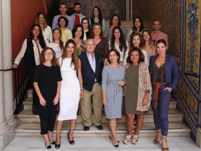 Una reunión formal en un edificio histórico, con una mezcla de hombres y mujeres vestidos de manera elegante, posando para una foto en una escalera decorada con azulejos.