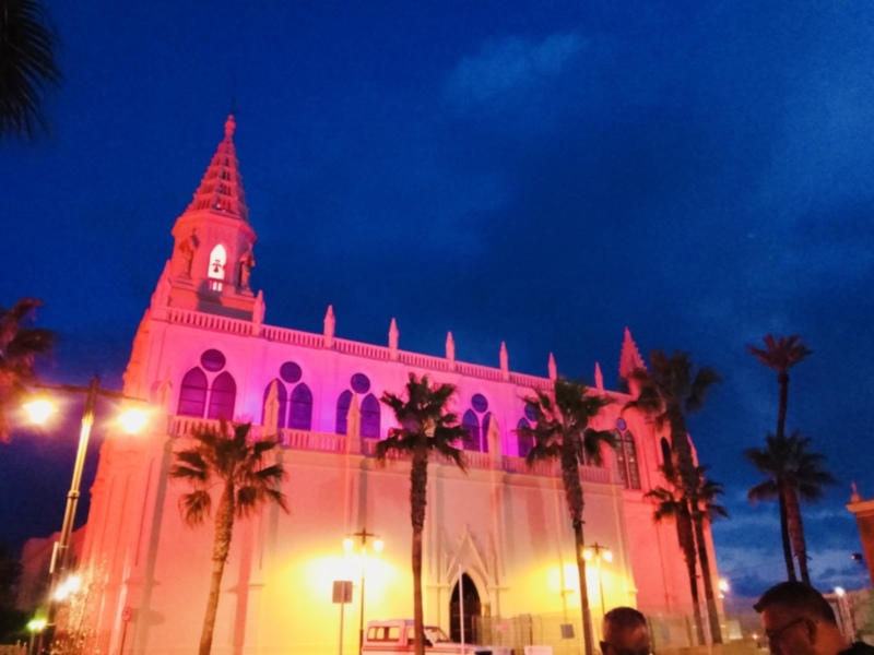 Illuminated church at dusk with palm trees in the foreground.
