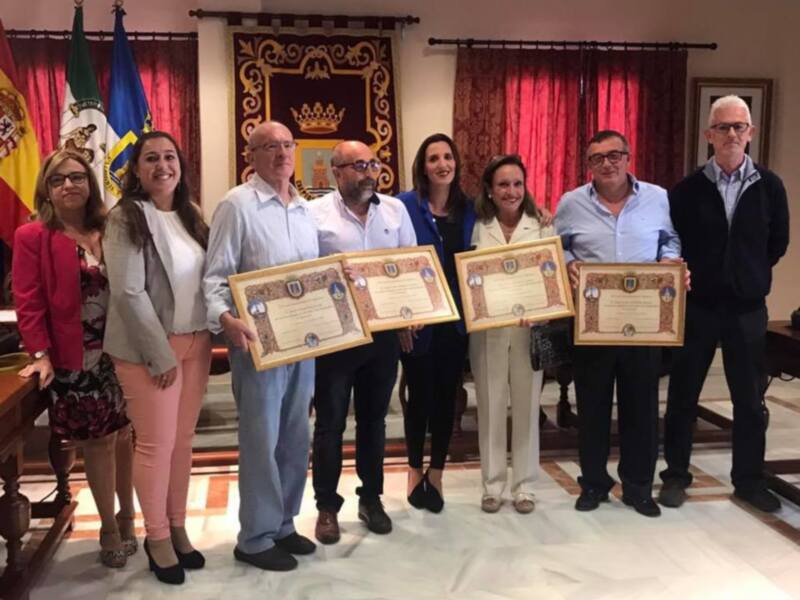 Una reunión formal en un salón con banderas y diplomas, donde personas están recibiendo reconocimientos.