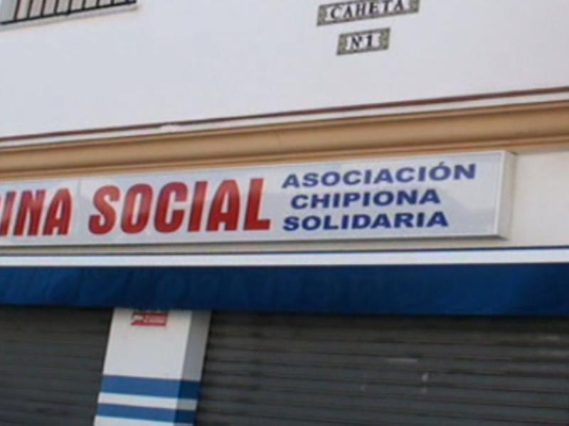 La fachada de una cocina social ubicada en Chipiona, Andalucía. La señalización indica que es un espacio destinado a la asistencia social y solidaria, probablemente para ofrecer comidas gratuitas o baratas a personas en situación de necesidad.
