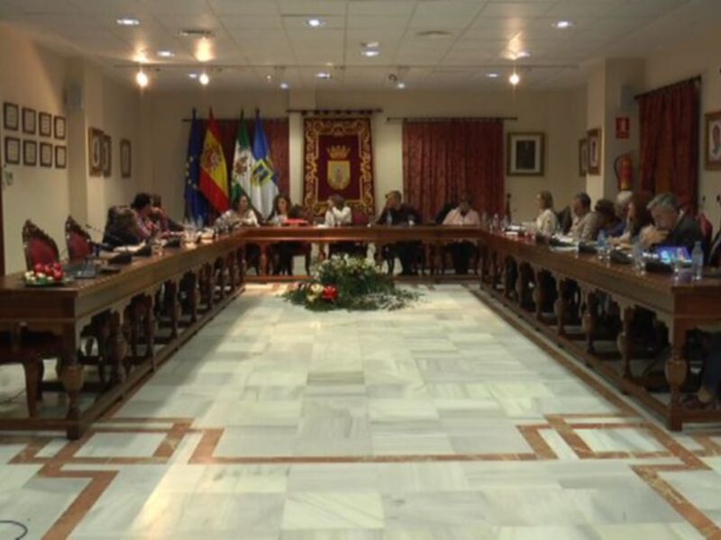 Sala de reuniones con mesas largas, sillas, banderas españolas y murales.
