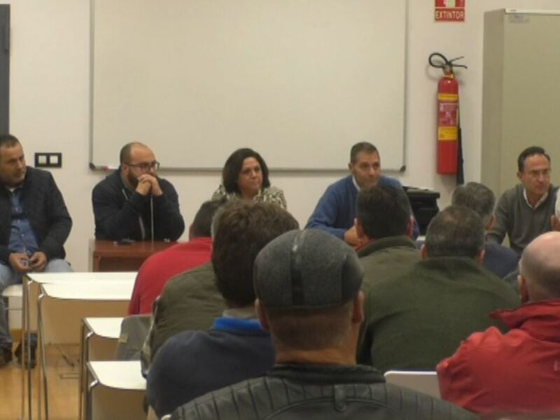 Reunión de trabajo en una sala de conferencias con participantes sentados en círculo alrededor de un panel de discusión.