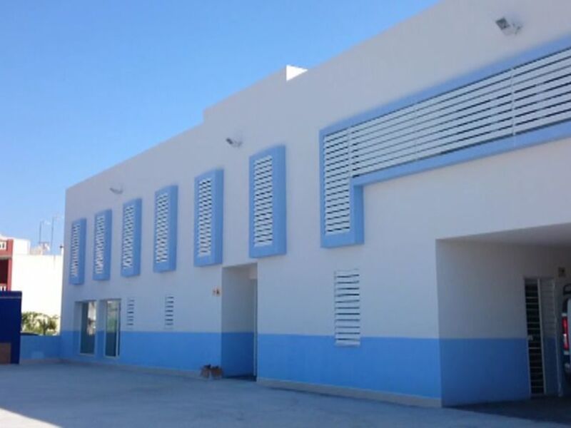 Fachada de un edificio industrial con ventanas azules y detalles blancos, bajo un cielo despejado.